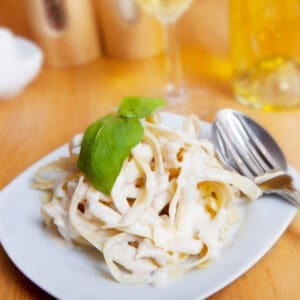 Plate of pasta topped with creamy cashew alfredo sauce and fresh basil, set on a wooden table with a fork and spoon beside it.