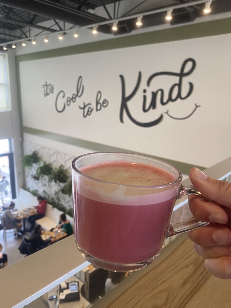 A hand holds a pink beverage in a glass mug from the top floor overlooking Kind Cafe, Vancouver.