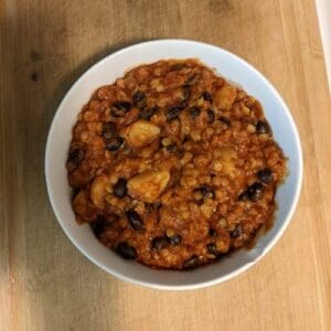 Bowl of hearty bean and lentil chili made with red wine, resting on a wood table.