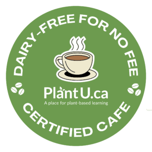 Green circular decal reading 'Dairy-Free For No Fee Certified Cafe' with an illustration of a steaming coffee cup in the center. Below the cup is the text 'PlantU.ca - A place for plant-based learning,' surrounded by small coffee bean icons.